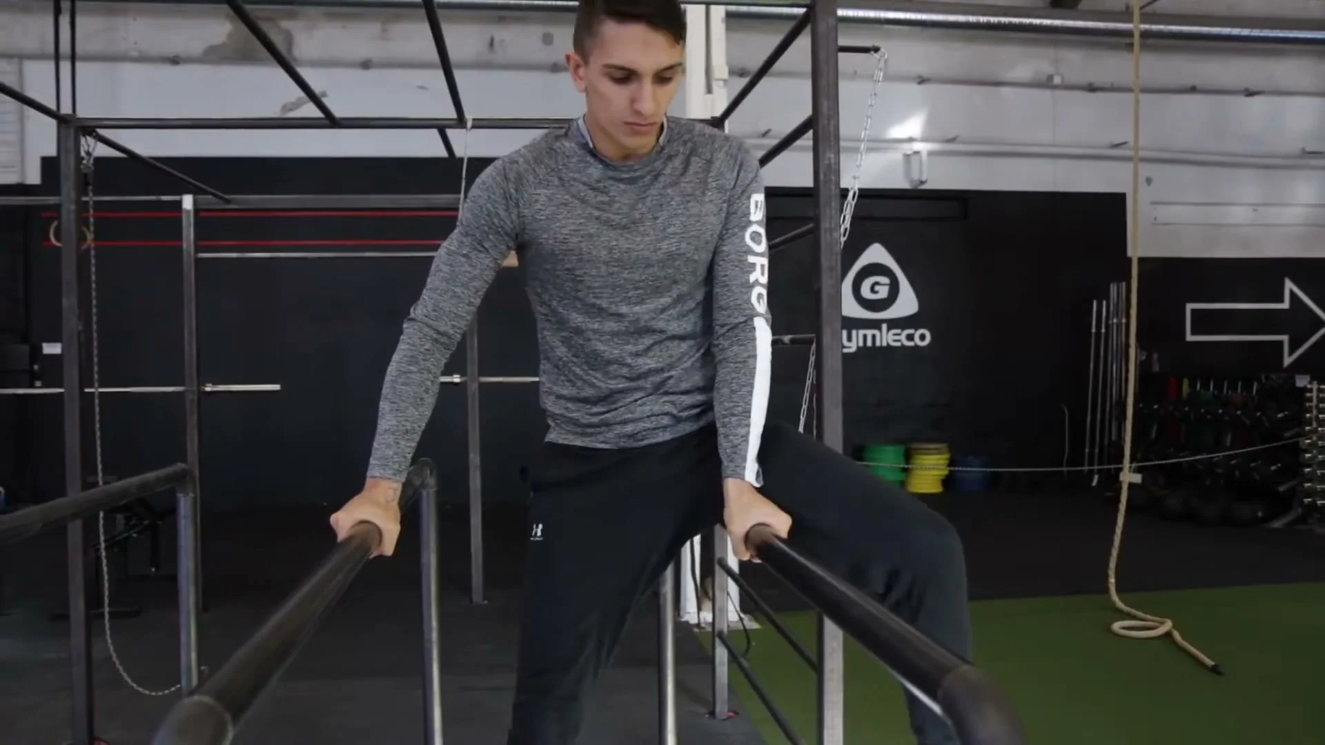 Step 3 of the one leg 360: inside leg coming out to the other side, sitting on the parallel bar with one hand released