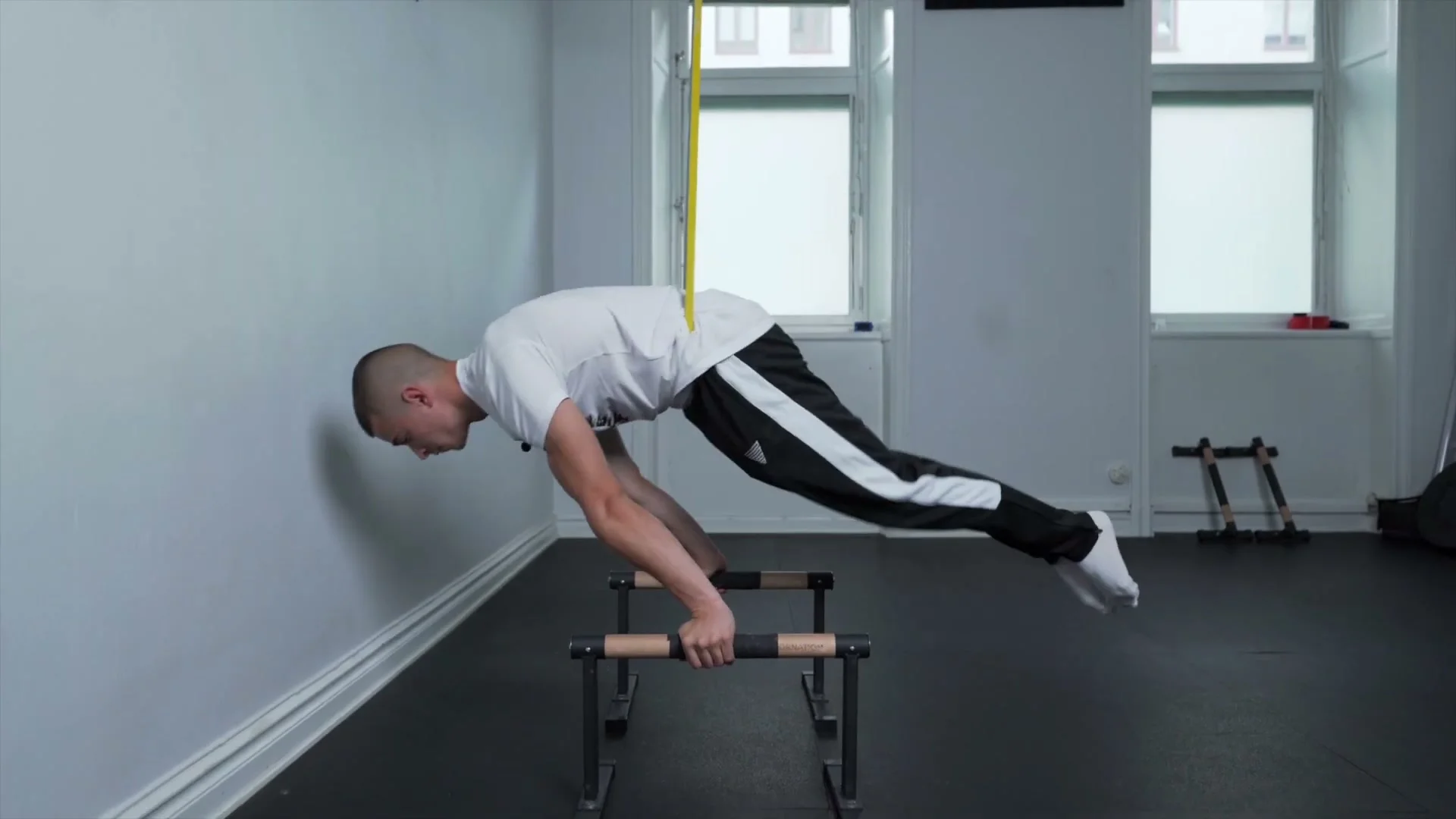 Daniel Hristov performing the tuck to full planche portion of the combo exercise on parallettes with a yellow elastic band for assistance: body in a full planche position, demonstrating the advanced combo exercise