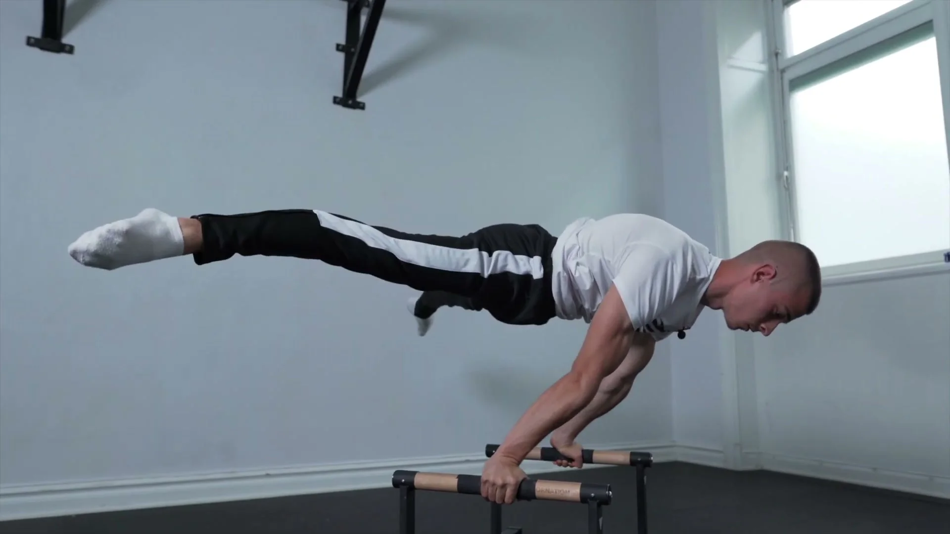 Daniel Hristov in a straddle planche position on parallettes after completing the handstand negative: body horizontal with legs spread wide, demonstrating the hold position at the bottom of the negative