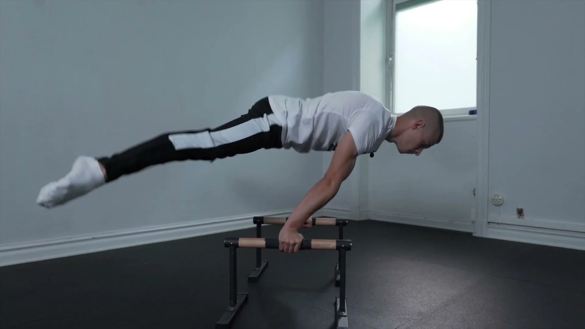 Daniel Hristov holding a straddle planche on parallettes: body horizontal with straight arms, legs spread wide, demonstrating the advanced hold that these five exercises build toward